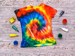 T-shirt painted in the style of tie dye with colors on a wooden background. Flat lay.