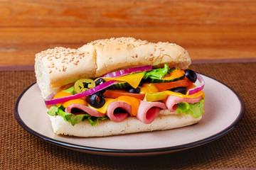 Sandwich with meat, cheese and fresh vegetables, closed, on wooden background