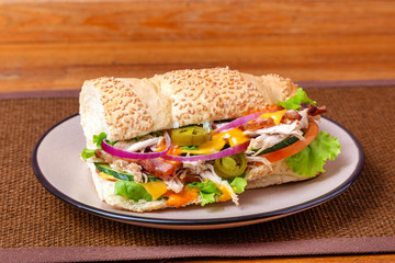 Sandwich with meat, cheese and fresh vegetables, closed, on wooden background