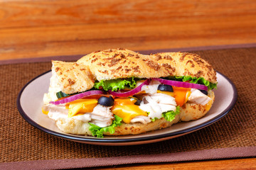 Sandwich with meat, cheese and fresh vegetables, closed, on wooden background