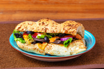 Sandwich with meat, cheese and fresh vegetables, closed, on wooden background