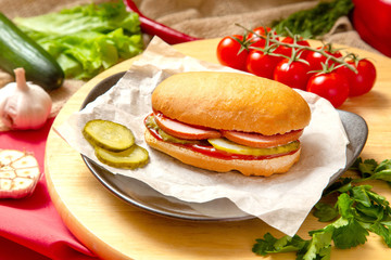 Sandwich with meat, cheese and fresh vegetables, closed, on wooden background
