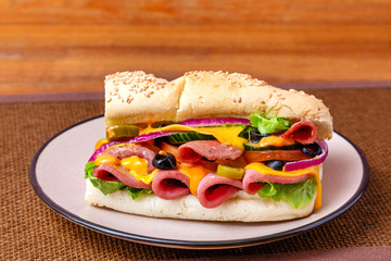 Sandwich with meat, cheese and fresh vegetables, closed, on wooden background