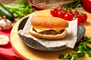 Sandwich with meat, cheese and fresh vegetables, closed, on wooden background