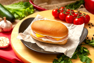 Sandwich with meat, cheese and fresh vegetables, closed, on wooden background