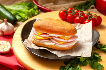 Sandwich with meat, cheese and fresh vegetables, closed, on wooden background