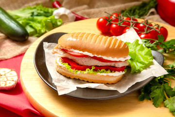 Sandwich with meat, cheese and fresh vegetables, closed, on wooden background
