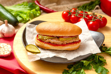 Sandwich with meat, cheese and fresh vegetables, closed, on wooden background