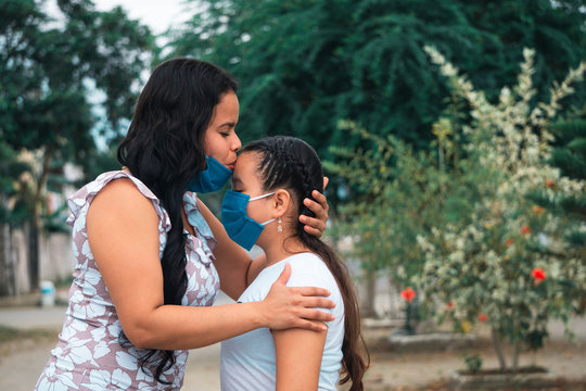 Mamá con mascarilla besando a su hija en la frente en el día de la madre al aire libre
