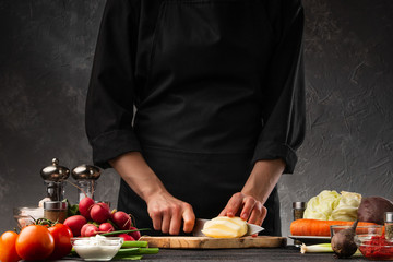 Chef cooks a dish with potatoes, slicing and cystitis. Against the background of vegetables, preparing French fries. Restaurant business, tasty and wholesome food