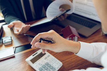 Business people home sales broker is using a pen pointing to the house model and describing the...