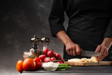 The chef cuts potatoes for cooking potatoes in French. Against the background of vegetables. With space for advertising, restaurant business, and cooking. Book of recipes