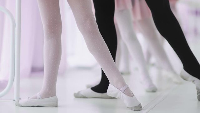 Little ballerinas in purple leotards training at barre.