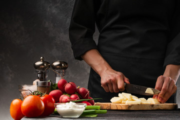 The chef cuts potatoes for cooking potatoes in French. Against the background of vegetables. With space for advertising, restaurant business, and cooking. Book of recipes