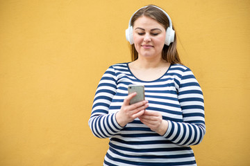 Pretty woman with a thin weight in headphones in a striped jacket on a background of orange wall