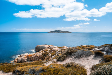 Orange rocks and small island near the ocean coastline against blue sky and white clouds in Australia