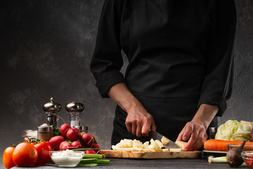The chef cuts potatoes for cooking potatoes in French. Against the background of vegetables. With space for advertising, restaurant business, and cooking. Book of recipes