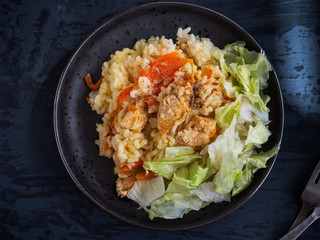 Hot breakfast with rice and meat on a ceramic black plate and iceberg salad tucked into small pieces