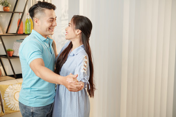 Beautiful young Asian man and woman looking at each other with love when dancing at home