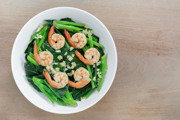 top view of stir fried chinese kale with shrimps in a ceramic bowl on wooden table. asian homemade style food concept.