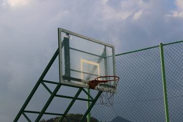 Fototapeta na wymiar basketball hoop against high green fence and blue sky