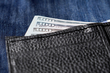 Black genuine leather wallet with banknotes inside, jeans background. Soft focus