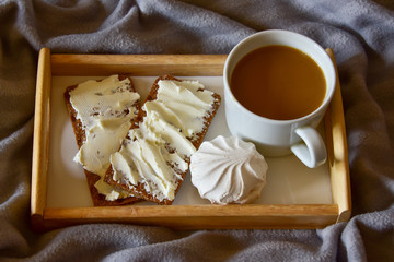 black coffee with marshmallows, bread rolls with butter, on a wooden tray. morning breakfast on a cozy plaid
