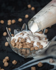 Light breakfast bran balls and yogurt in a glass bowl on a black background.
