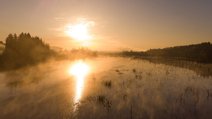Dawn on the lake, with steam in the forest. Morning landscape, with the rays of the sun. Shot from a height