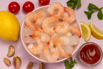 Tiger prawns with ice in a pink plate. Lemon, tomatoes, garlic and tomato sauce