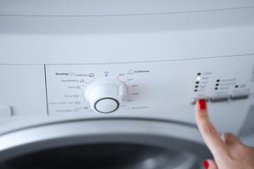 The girl sets the washing program for the washing machine.