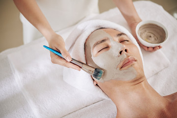 Asian man getting rejuvenating and moisturizing skin treatment at beauty salon