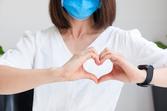 Young Asian woman with a medical mask on face makes a heart out of her hands. The concept of Thanks to health workers to cheer and love
