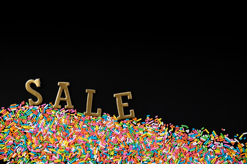 Colorful sprinkles with sale gold paper text on black background. Top view or flat lay. Concept design for banner, promotion, shopping sale