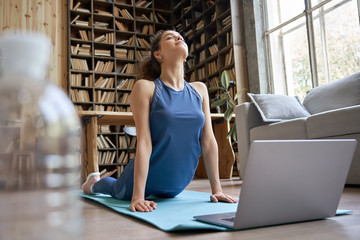 Happy fit sporty hispanic girl doing online yoga exercise stretch on mat at home. Active healthy latin woman enjoy sport pilates physical fitness training on laptop computer watching video class guide