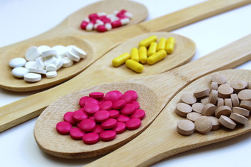 Five wooden spoons lie with pills on a gray background