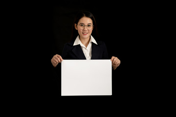 Fototapeta premium Beautiful asian business woman holding a blank paper sheet or white banner with both hands and smiling on black background