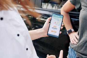 Female driver accepting request in car sharing application on her smartphone to share trip with...