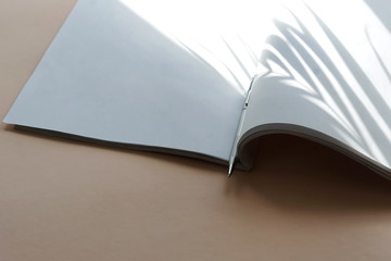 Open magazine mock up, pen  and floral shadows on beige background. copy space