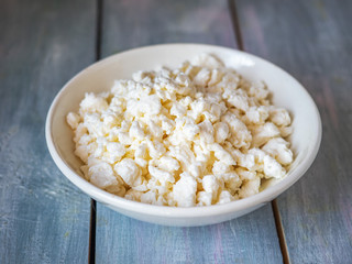 Fresh rustic cottage cheese in a white deep plate on a blue wooden table