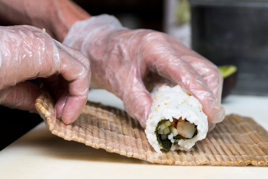 Close-up Of Chef's Hands Making A Sushi Roll On A Bamboo Mat With The Background Out Of Focus