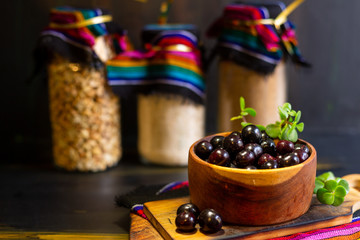 Blackcurrant, black berries for dessert, on a black table and in the background jars with seeds