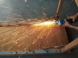 view of Grinder in hand cutting iron with fire spark on ground.