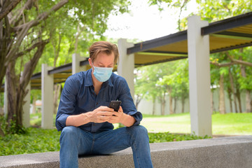 Obraz premium Young man with mask using phone and sitting at the park