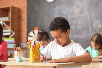 Cute African-American boy drawing at school