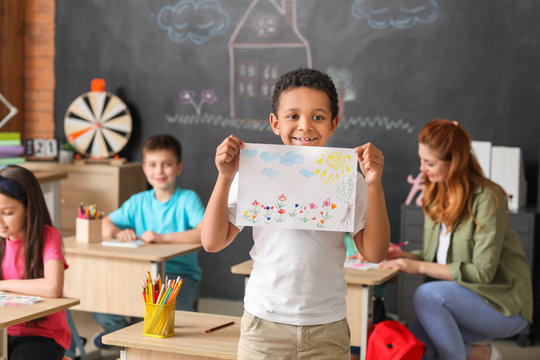 Cute African-American boy with drawing at school
