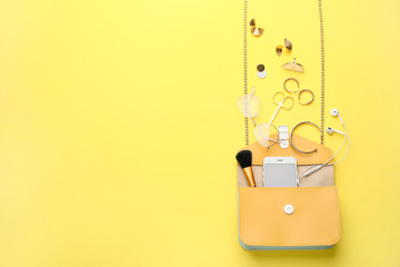 Stylish bag with female accessories and mobile phone on color background