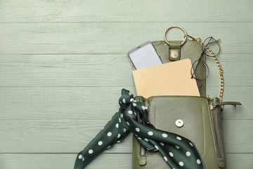 Stylish bag with female accessories and mobile phone on color wooden background