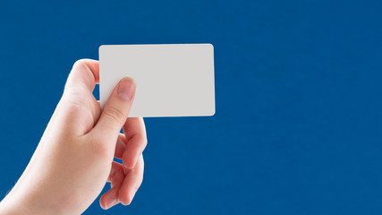 Close up of a female hand holding a blank white business card on a blue background. Business idea, copy space