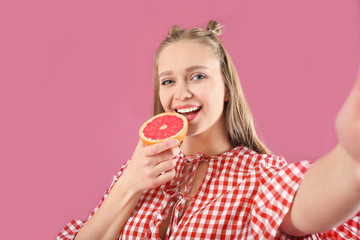 Young woman with grapefruit taking selfie on color background. Diet concept
